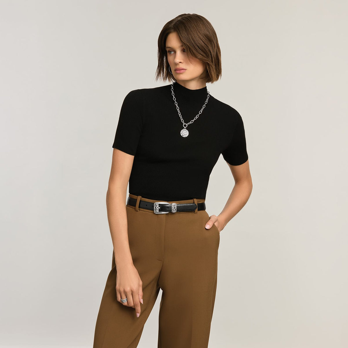 Model wearing a Brighton silver-tone chain necklace with hammered medallion pendant, styled with a Brighton black leather belt