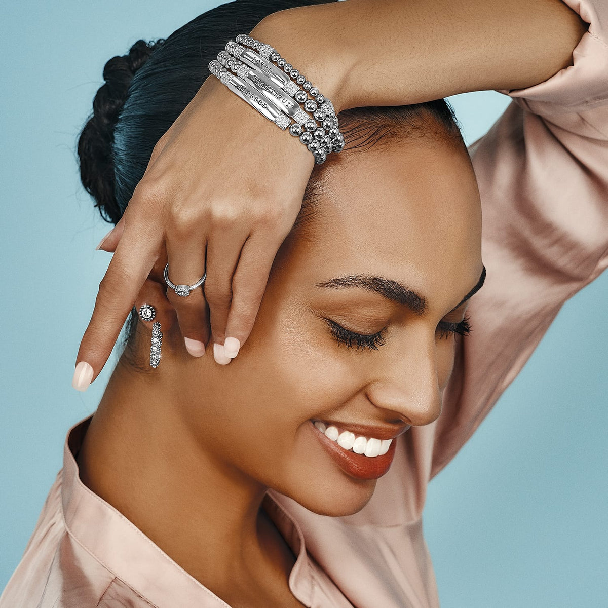 Model wearing stacked Brighton silver-plated beaded bracelets with engraved bars, paired with a crystal ring and earrings