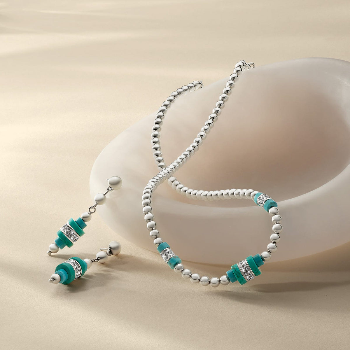 Brighton silver-plated beaded necklace and drop earrings with turquoise beads and crystal accents, styled with a ceramic dish