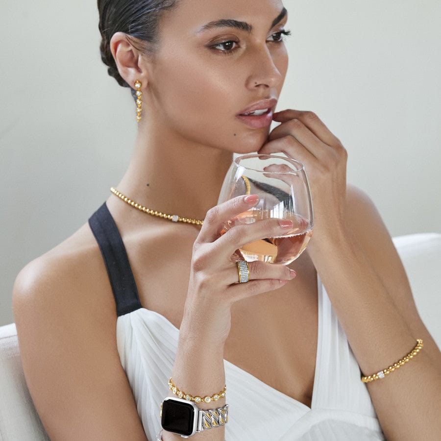 Model wearing Meridian Petite Stretch Bracelet in gold with matching necklace holding glass wtih beverage and looking right