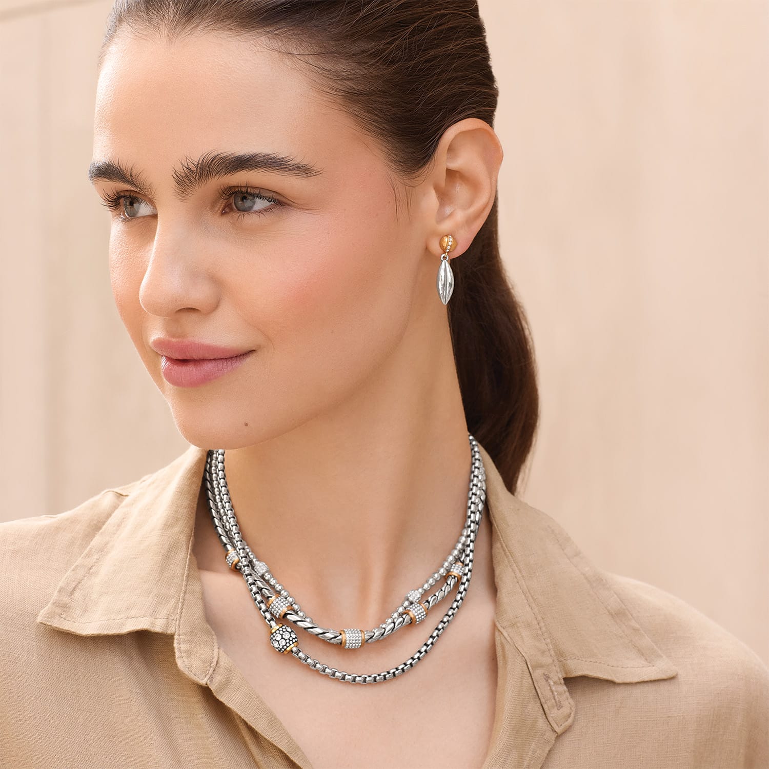 Model wearing a Brighton two-tone layered necklace with crystal accents paired with silver and gold drop earrings