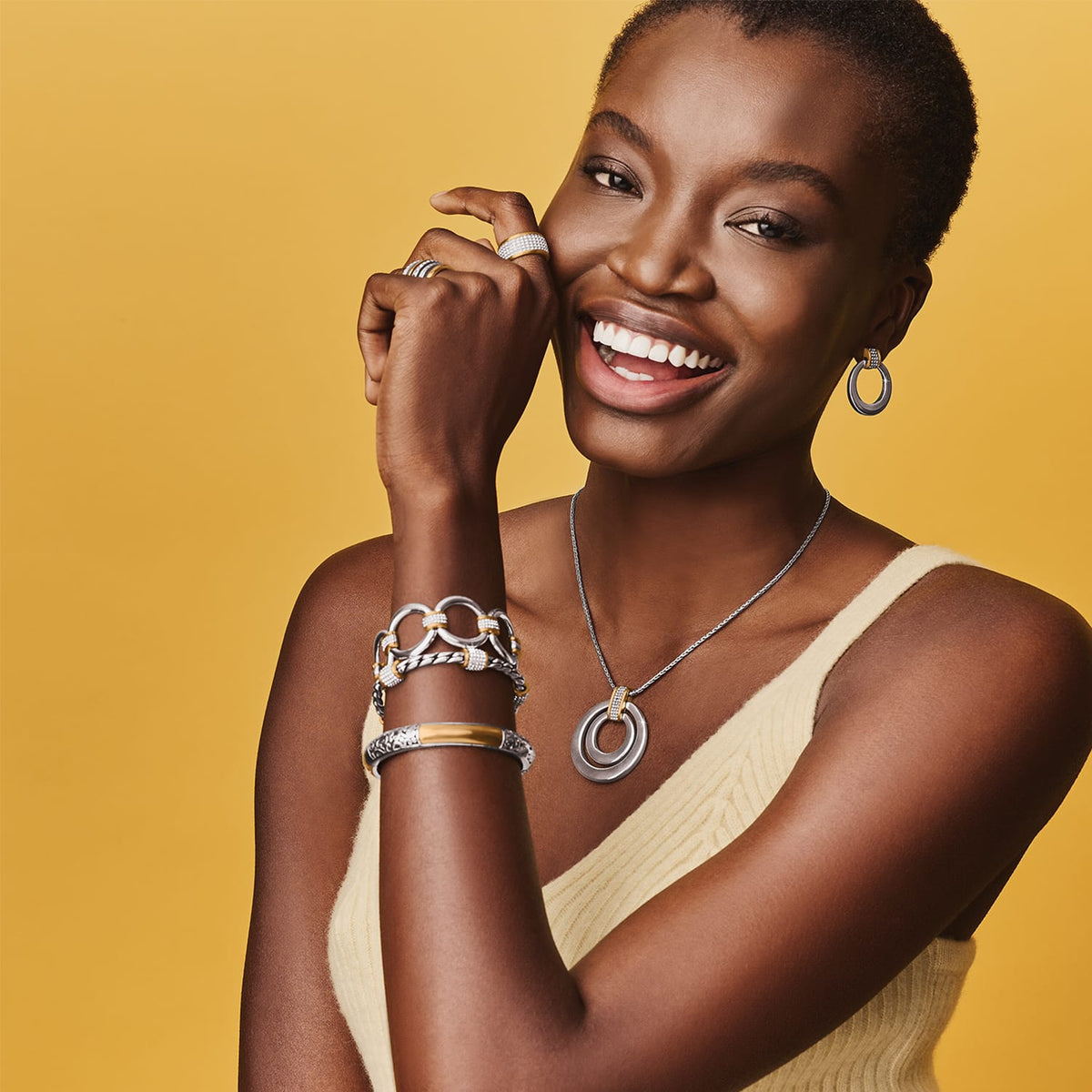 Model wearing a Brighton two-tone circle pendant necklace with coordinating Brighton accessories including bracelets, earrings, and rings