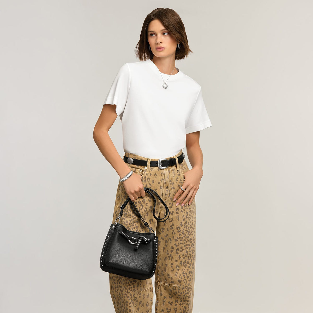 Model with a Brighton black leather bucket handbag featuring studded trim, knot detail, and adjustable crossbody strap