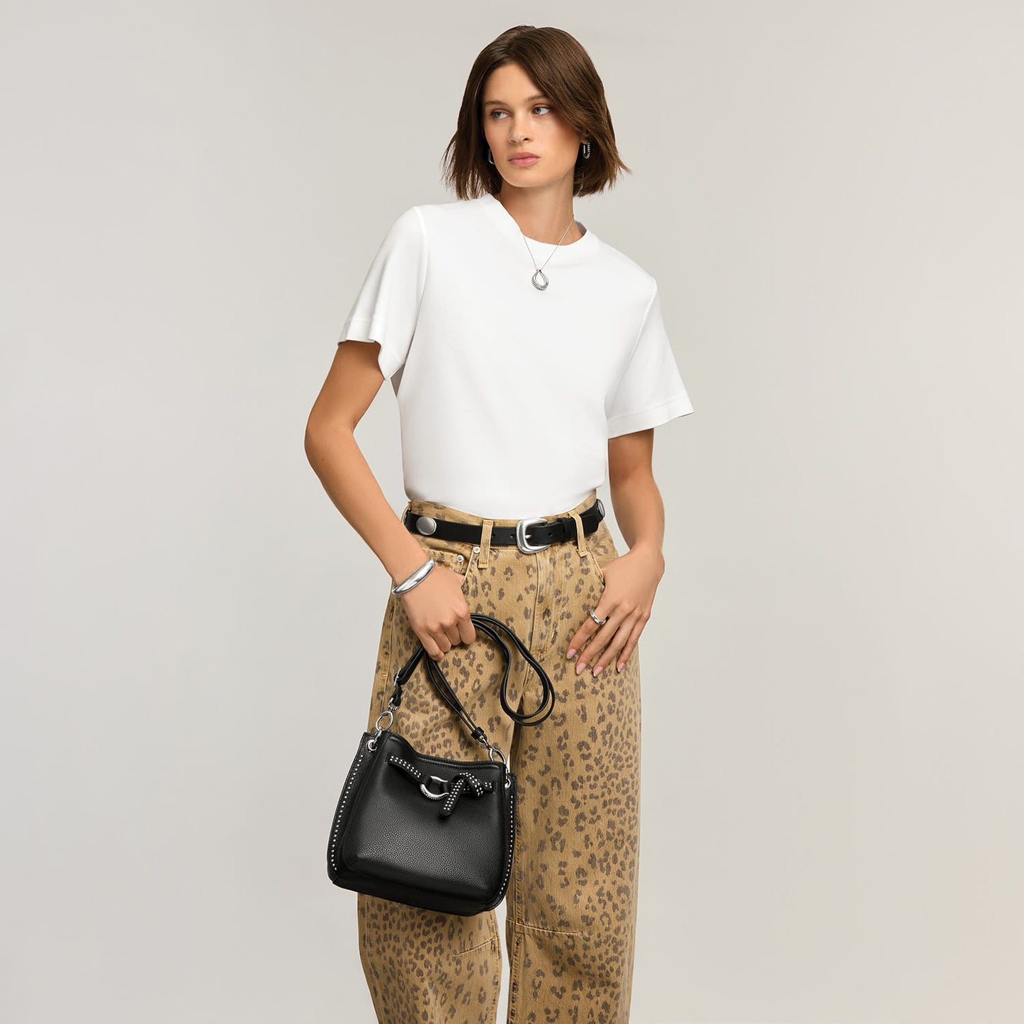 Model with a Brighton black leather bucket handbag featuring studded trim, knot detail, and adjustable crossbody strap