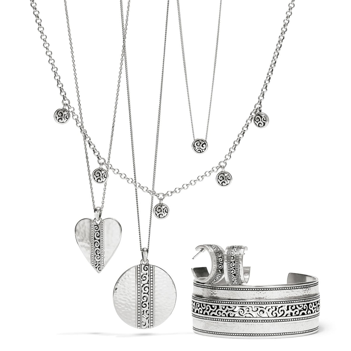 Brighton silver-plated jewelry set styled with layered heart and disc pendant necklaces, hoop earrings, and scroll-detailed cuff bracelet