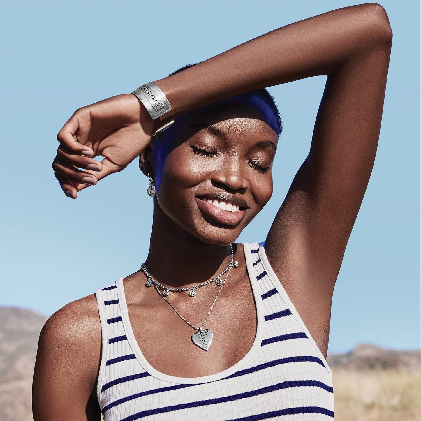 Model wearing a Brighton silver-plated heart pendant necklace with layered medallion choker and coordinating Brighton accessories