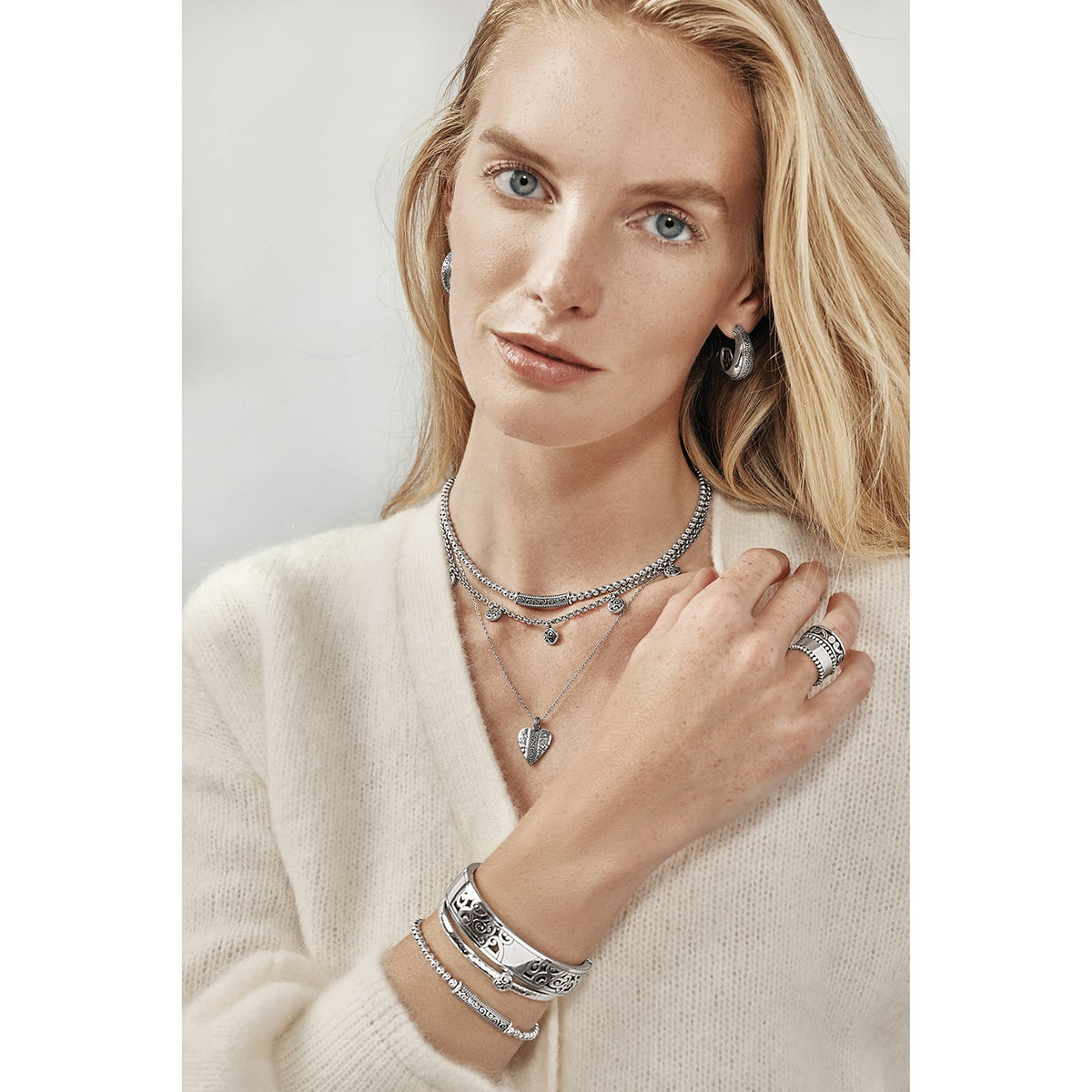 Model wearing Brighton silver-plated layered necklaces with pendants and coordinating Brighton accessories including hoop earrings, rings, and bracelets