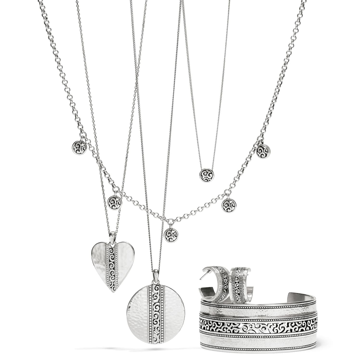 Brighton silver-plated jewelry set styled with layered scroll pendant necklaces, hoop earrings, and engraved cuff bracelet on white background