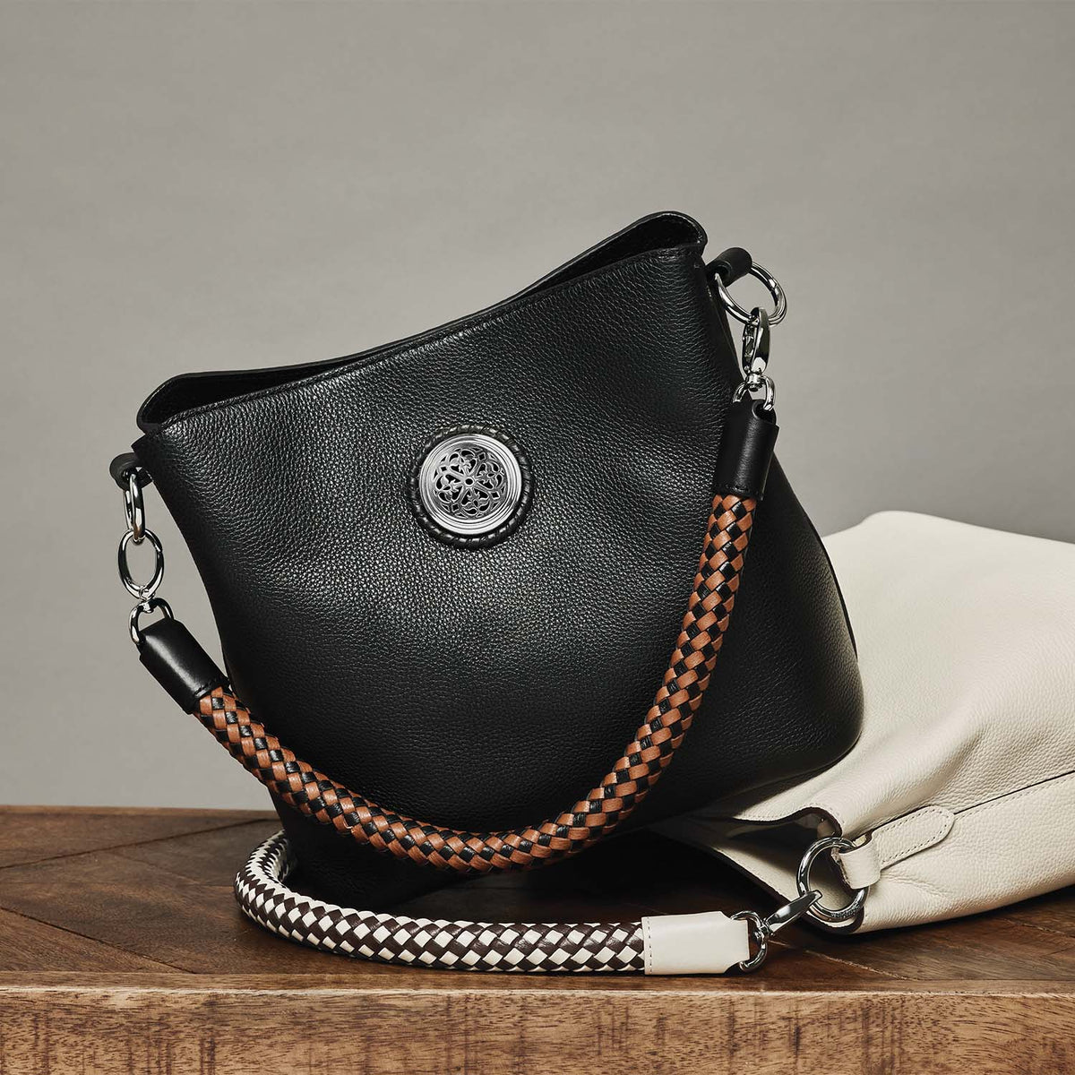 Brighton black leather handbag styled with a white leather bag and braided straps on a wooden surface
