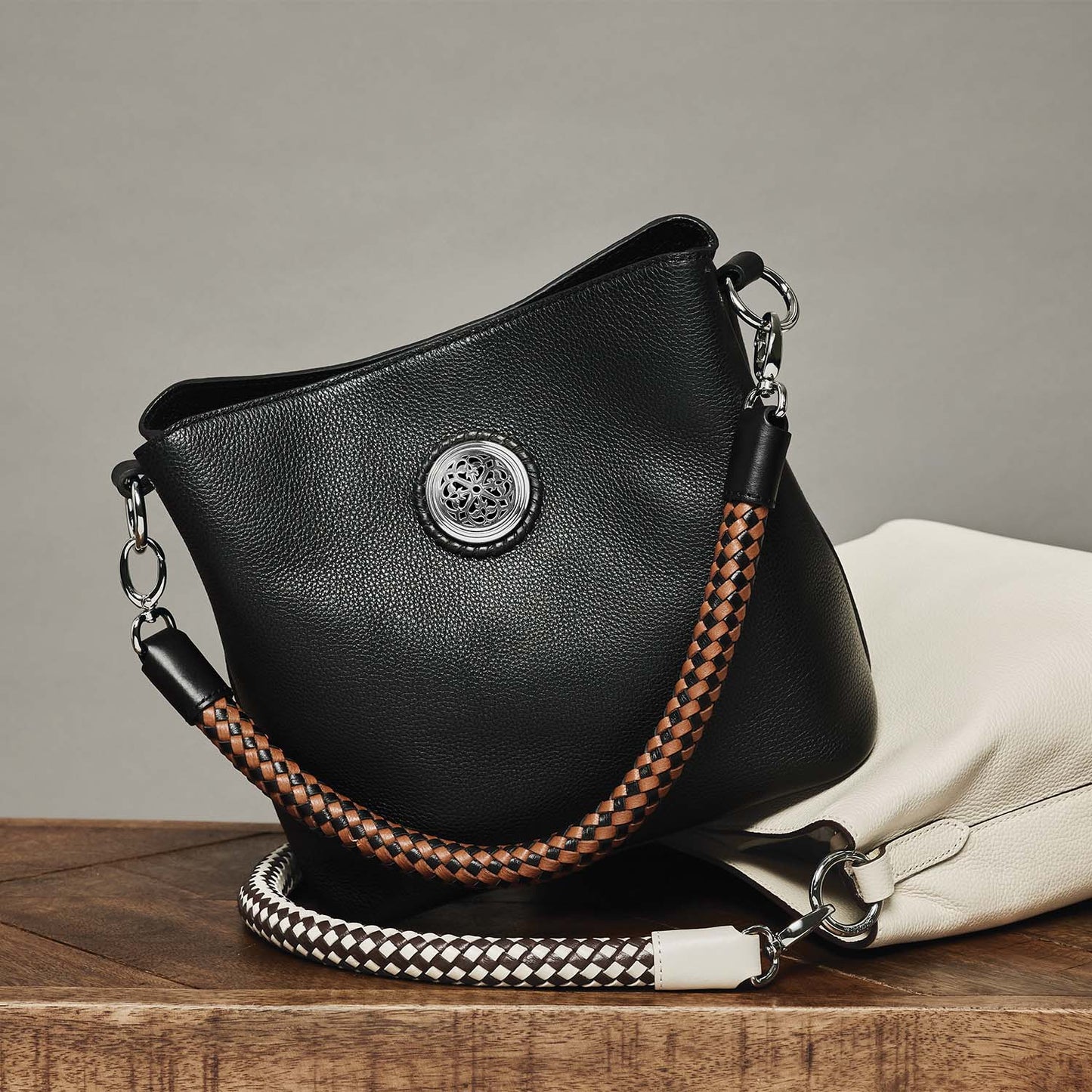 Brighton black leather handbag styled with a white leather bag and braided straps on a wooden surface