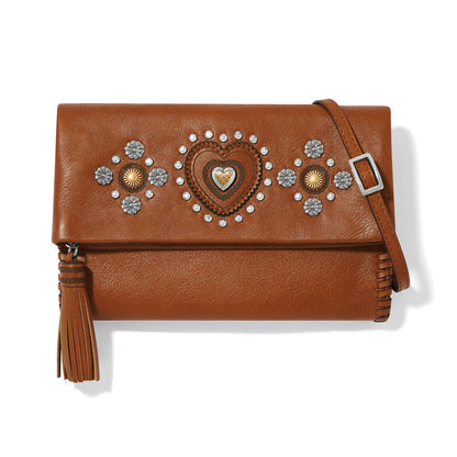 Brighton brown leather crossbody handbag with heart and floral studded accents, tassel, and adjustable strap on a white background