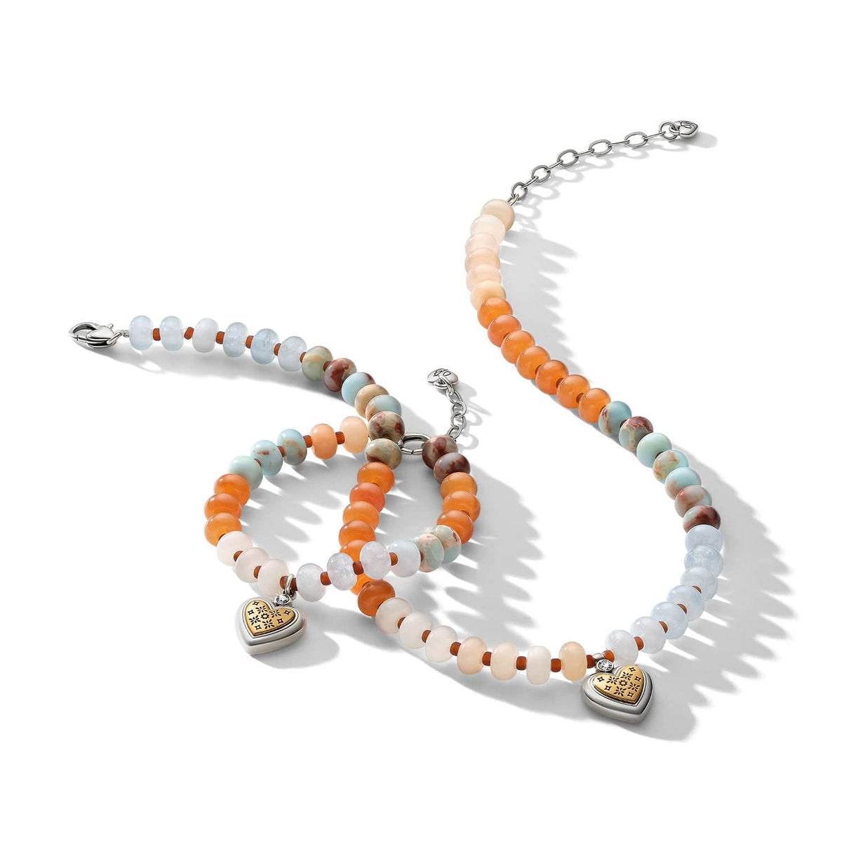 Brighton beaded necklace and bracelets with orange, blue, and cream stones featuring two-tone heart charms on a white background