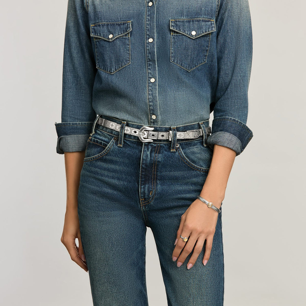Model wearing a Brighton leather belt with silver-tone engraved plaques and horseshoe buckle, paired with a Brighton bracelet