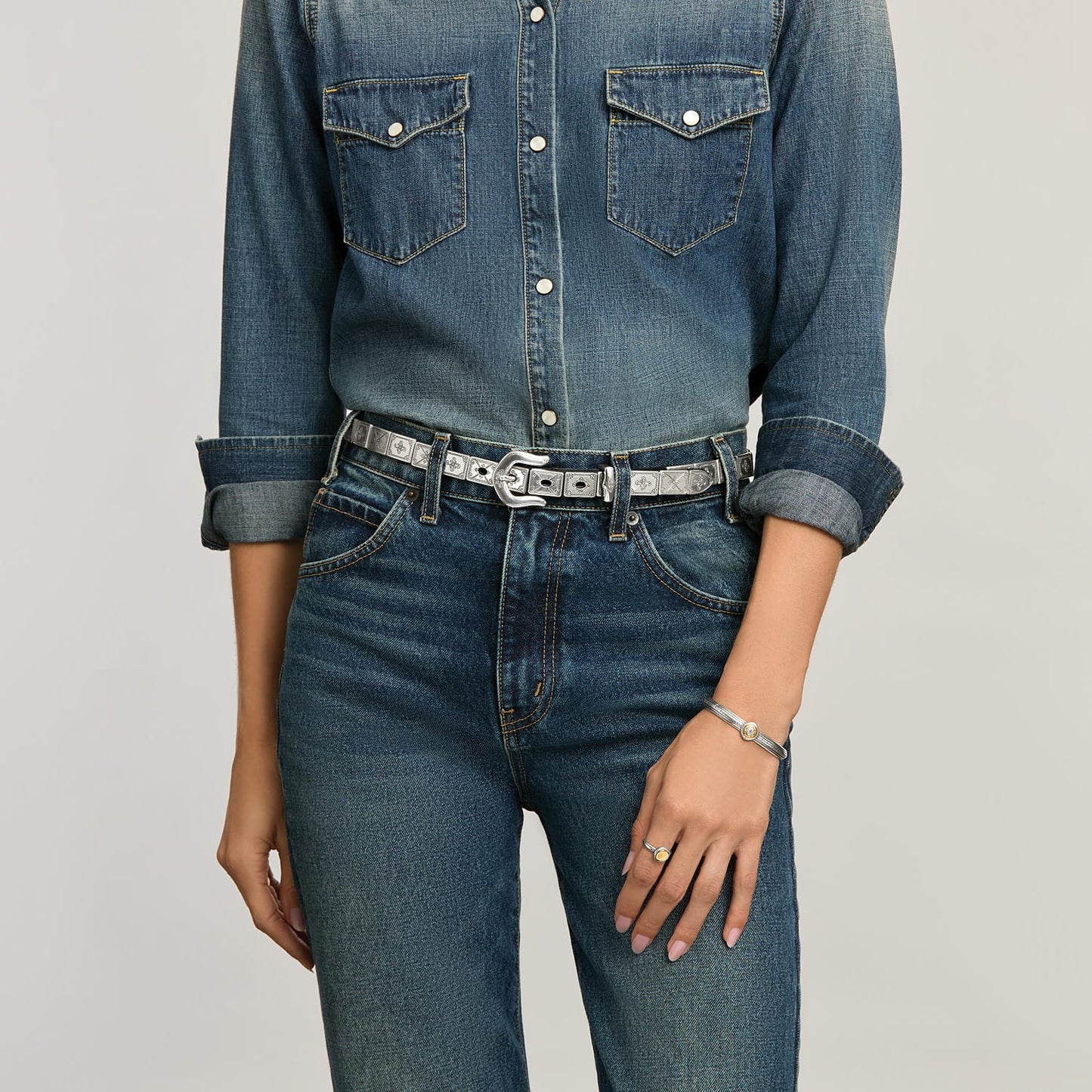 Model wearing a Brighton leather belt with silver-tone engraved plaques and horseshoe buckle, paired with a Brighton bracelet