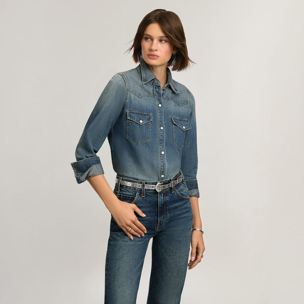 Model wearing a Brighton silver-tone studded leather belt with ornate buckle, paired with denim shirt and jeans