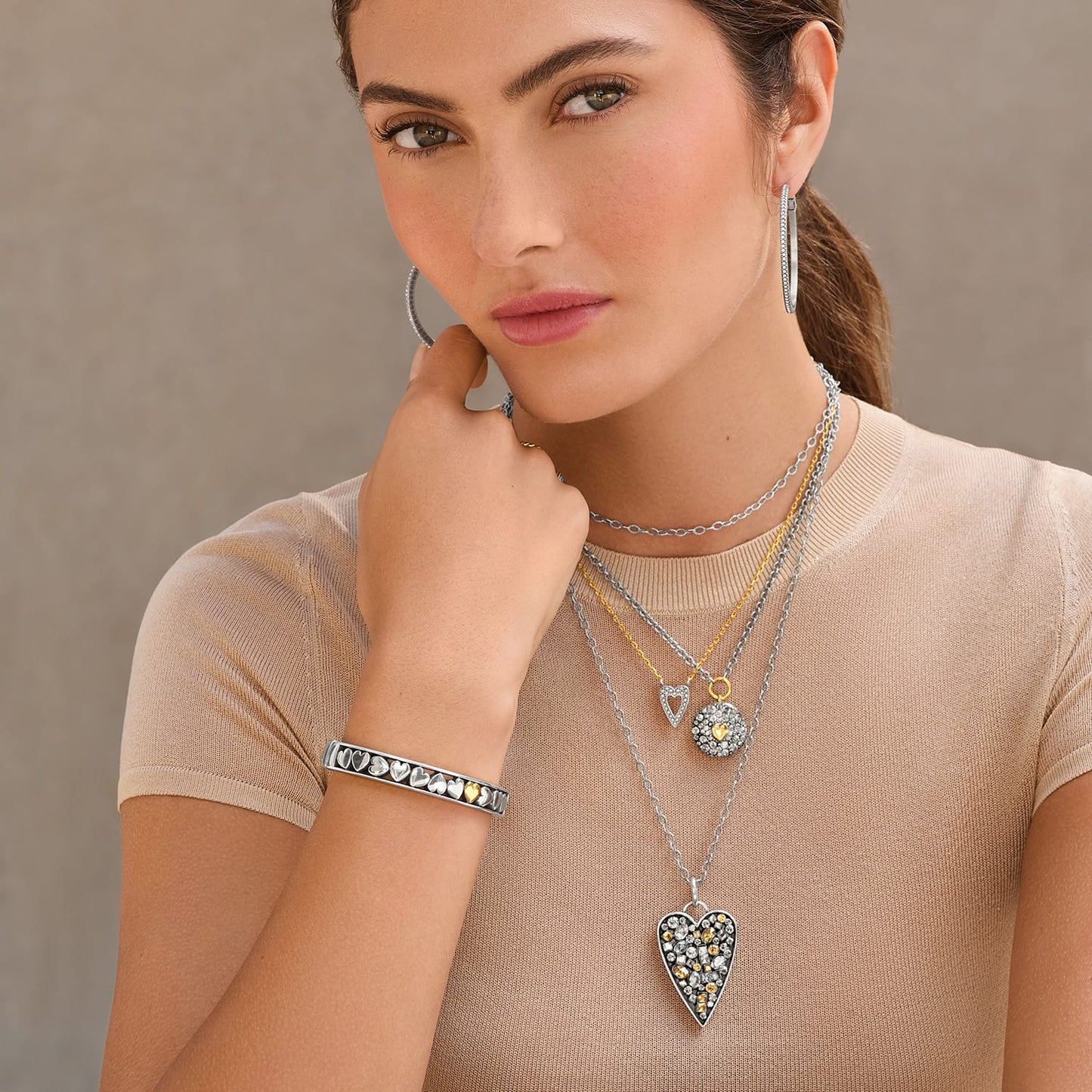 Model wearing Brighton two-tone heart pendant necklaces with crystals, silver hoop earrings, and coordinating Brighton bracelet