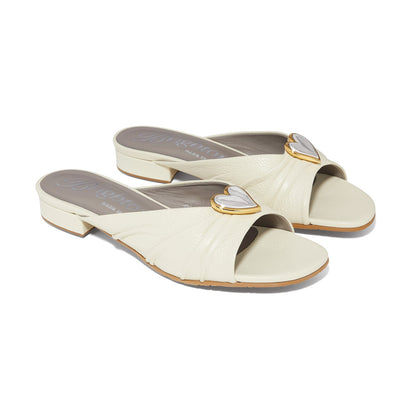 Brighton slide sandals in cream leather with silver and gold-tone heart medallion accents on a white background