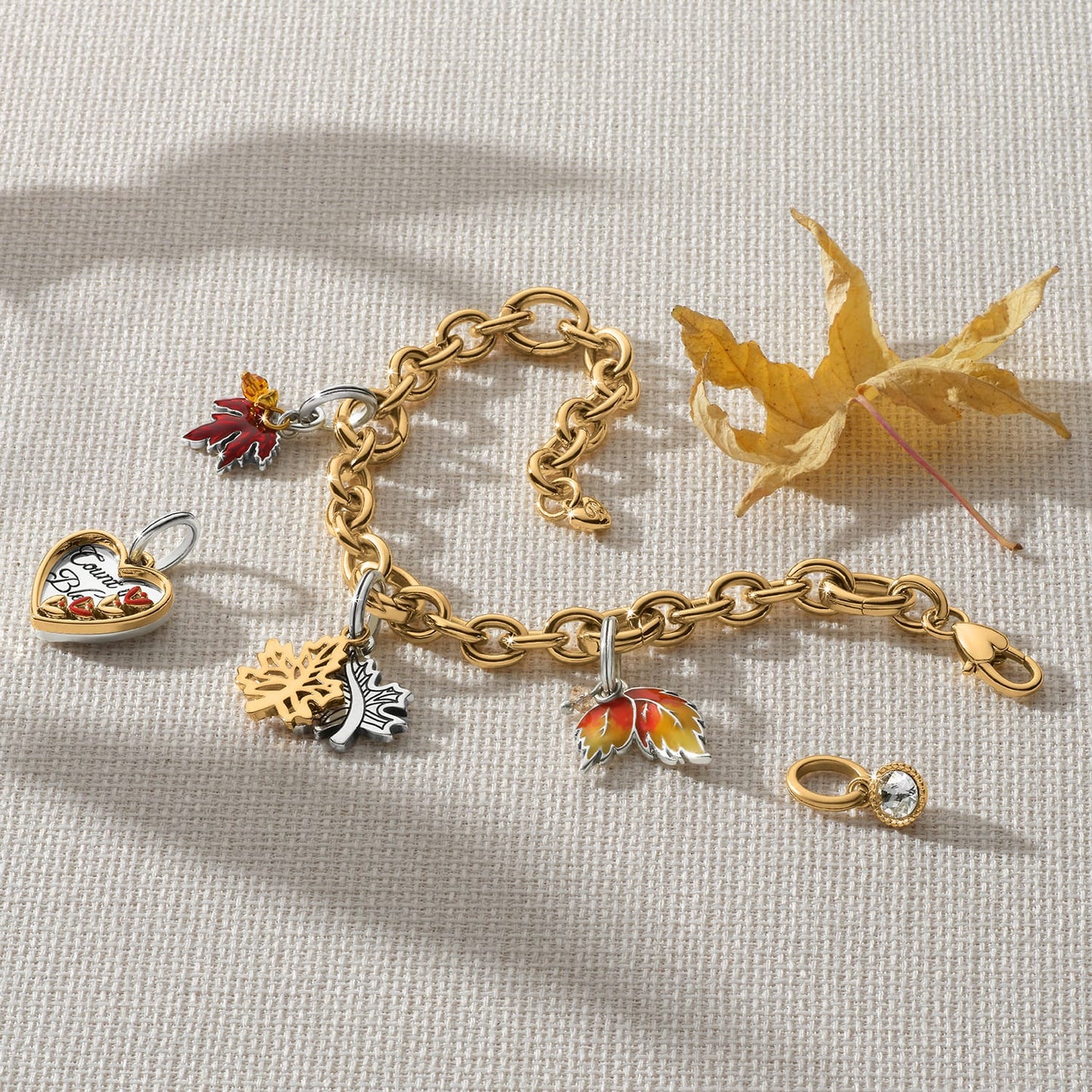 Brighton two-tone charm bracelet styled with maple leaf charms and dried autumn leaves on woven fabric