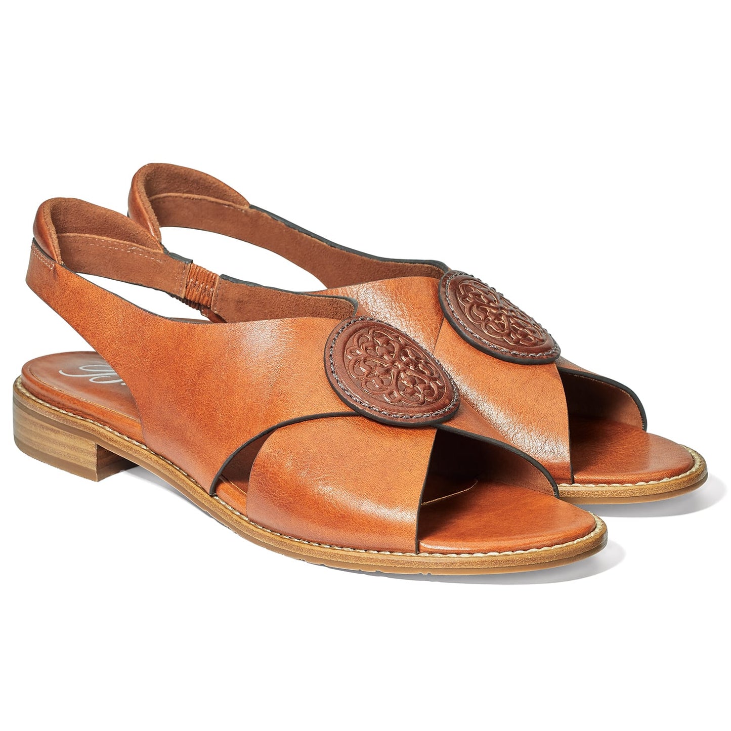 Brighton slingback sandals in tan leather with crossover straps and embossed medallion accents on a white background