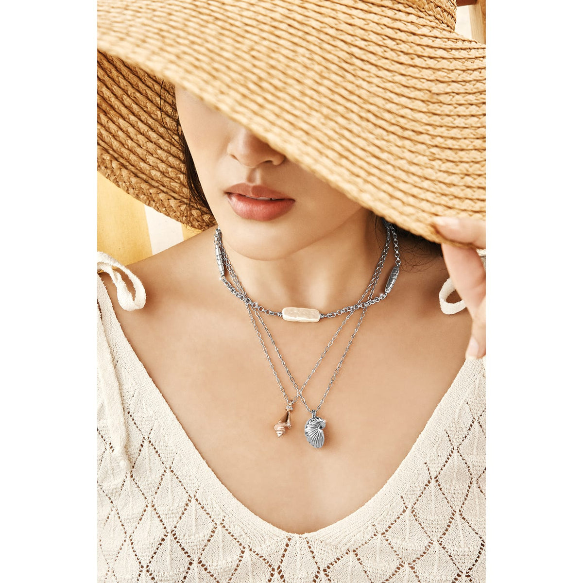 Model wearing layered Brighton silver-plated necklaces with pearl bar, seashell, and conch shell pendants