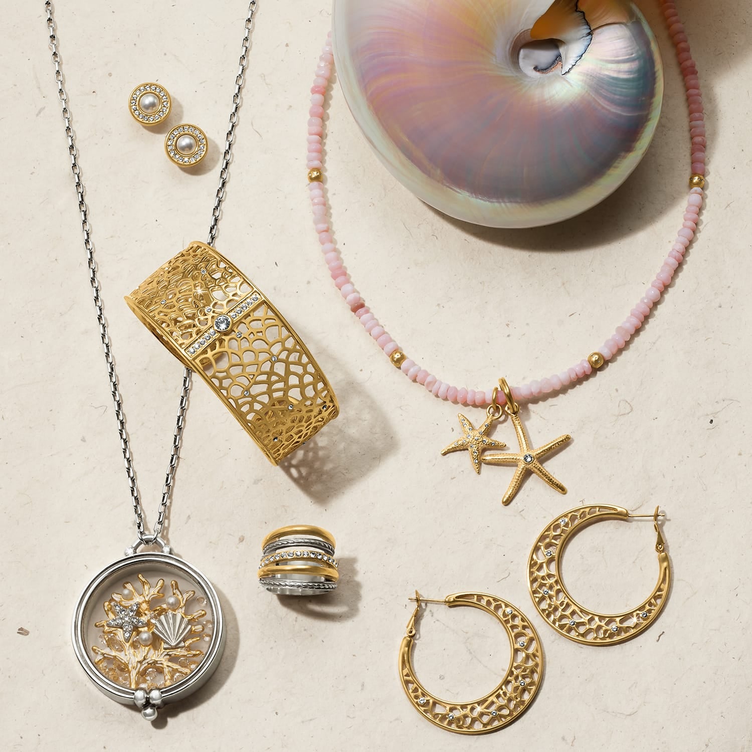 Brighton jewelry collection styled with a nautilus shell and pink beaded necklace on a neutral background