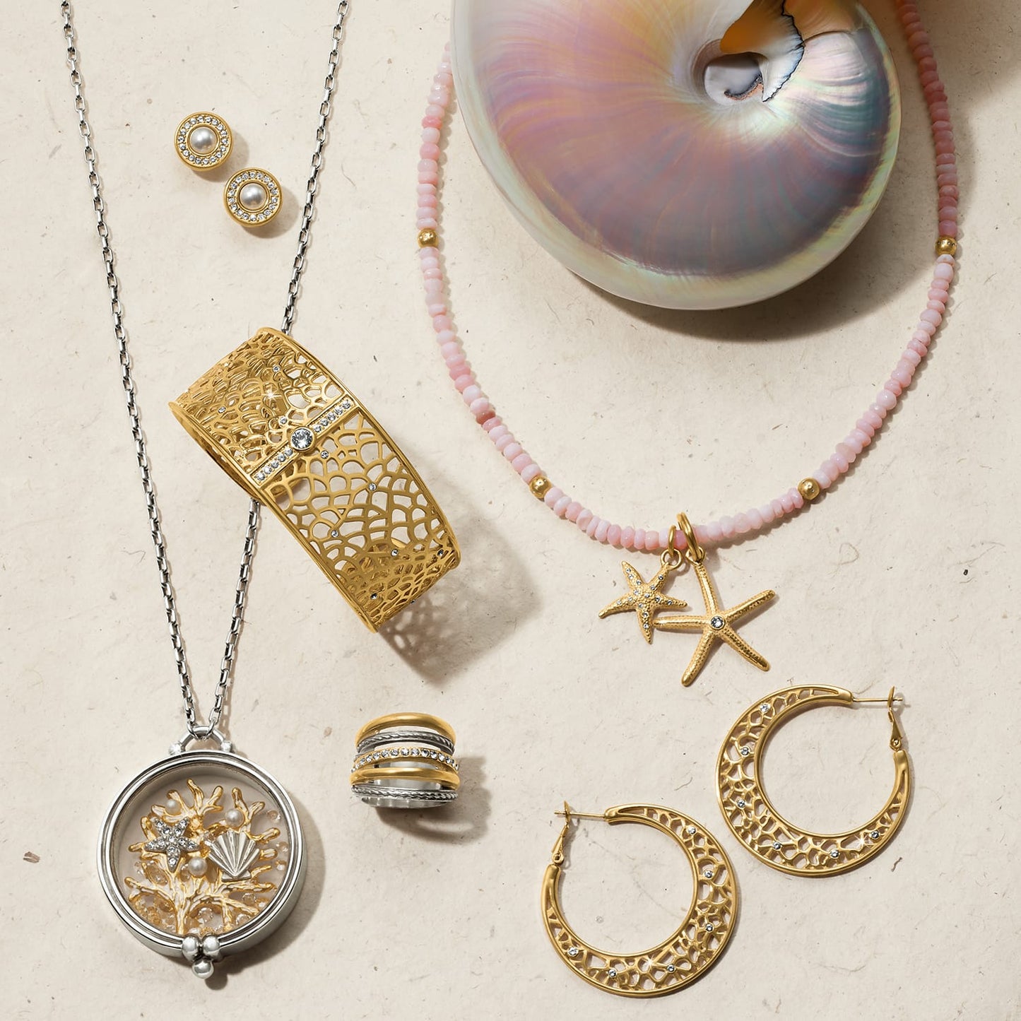 Brighton jewelry collection styled with a nautilus shell and pink beaded necklace on a neutral background