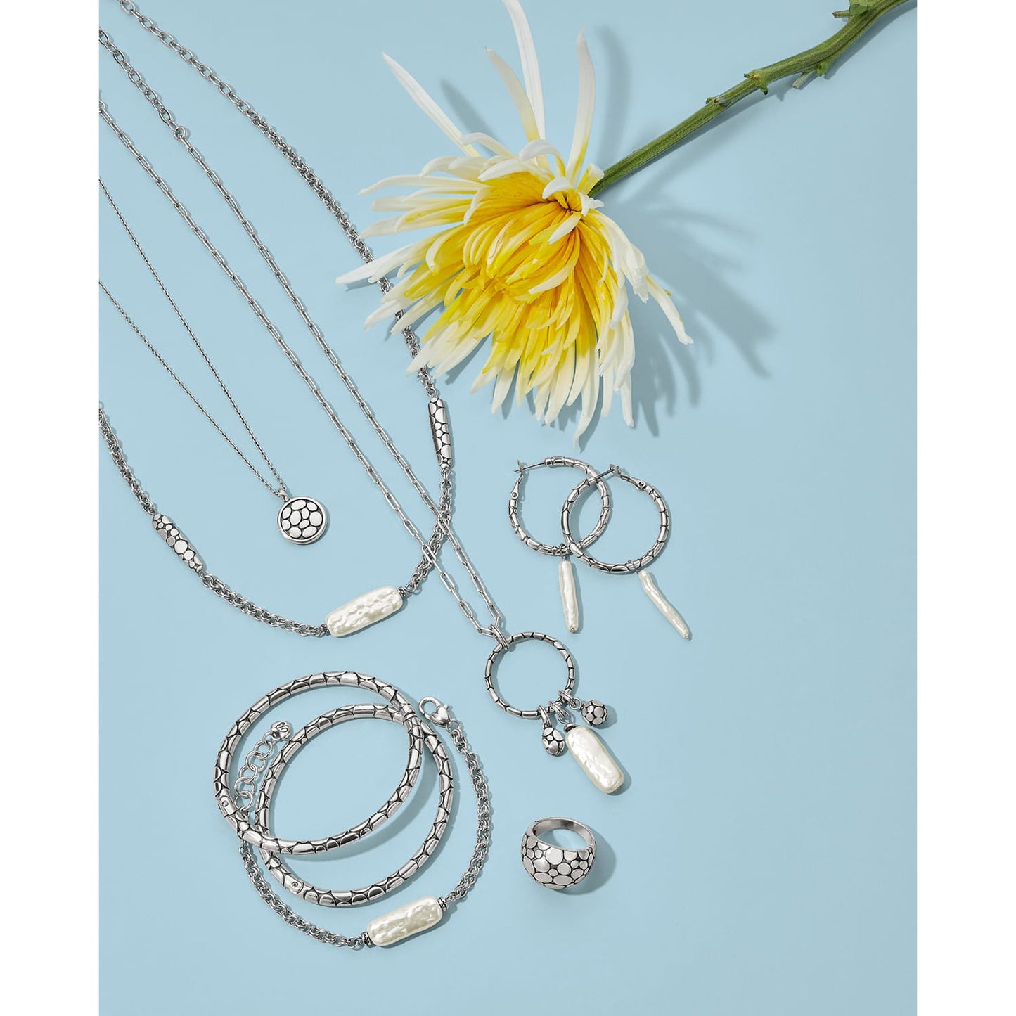 Brighton silver-plated jewelry set styled with a yellow chrysanthemum flower and pearl accents on a blue background