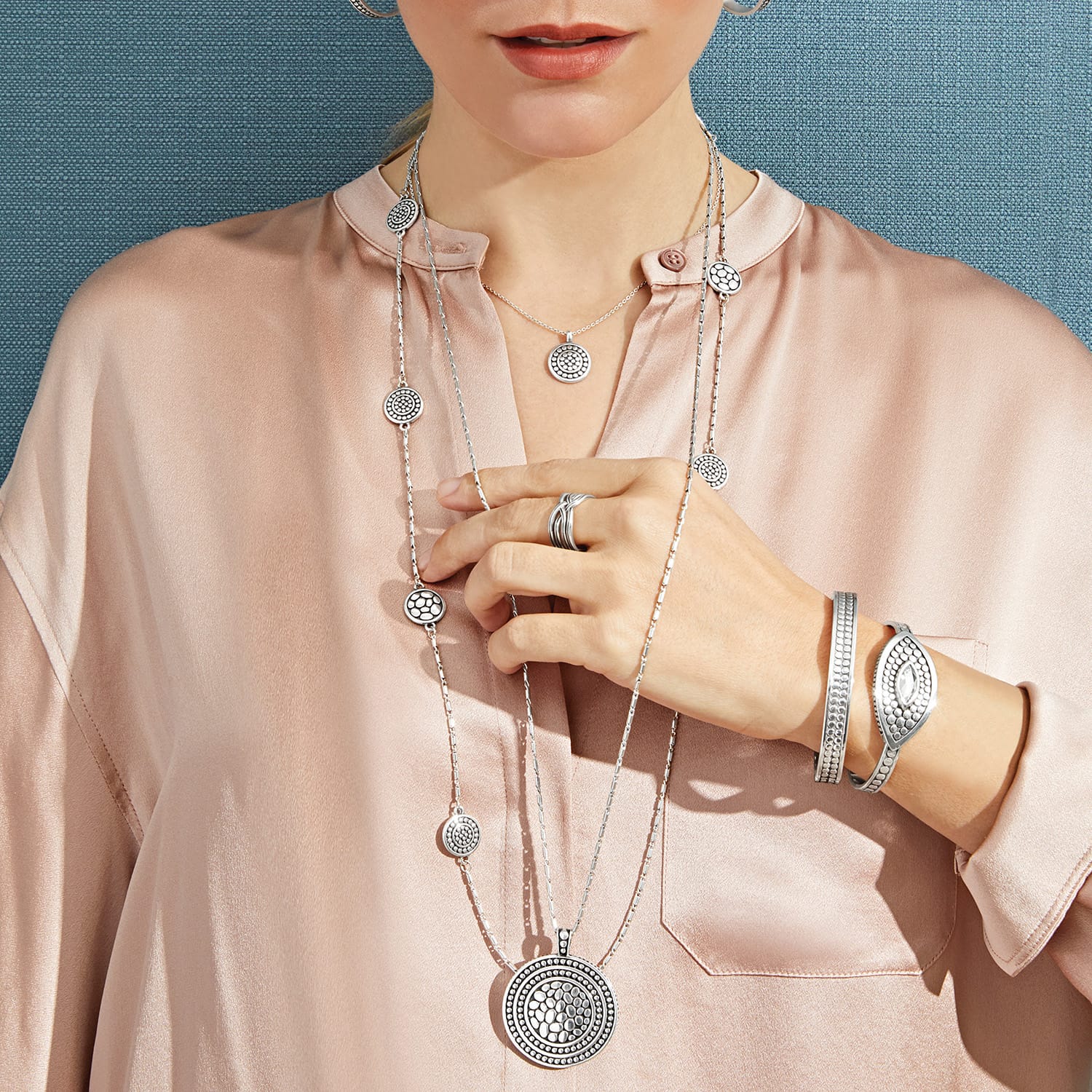 Model wearing layered Brighton silver-plated medallion necklaces with coordinating Brighton accessories including rings and bangle bracelets