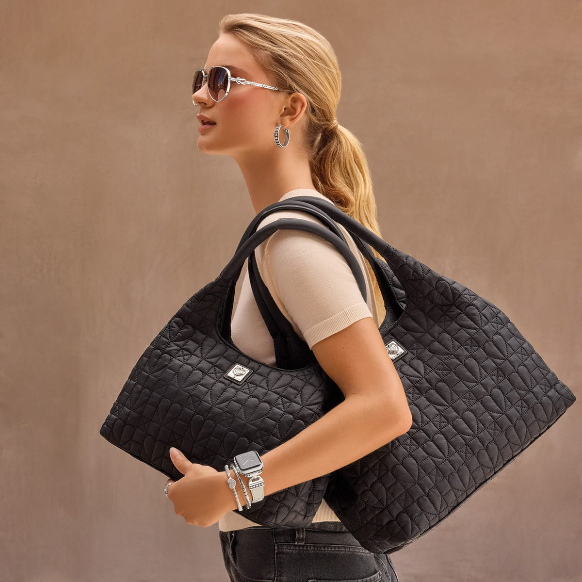 Model with a Brighton black quilted heart-pattern tote handbag and coordinating Brighton accessories including sunglasses and watch
