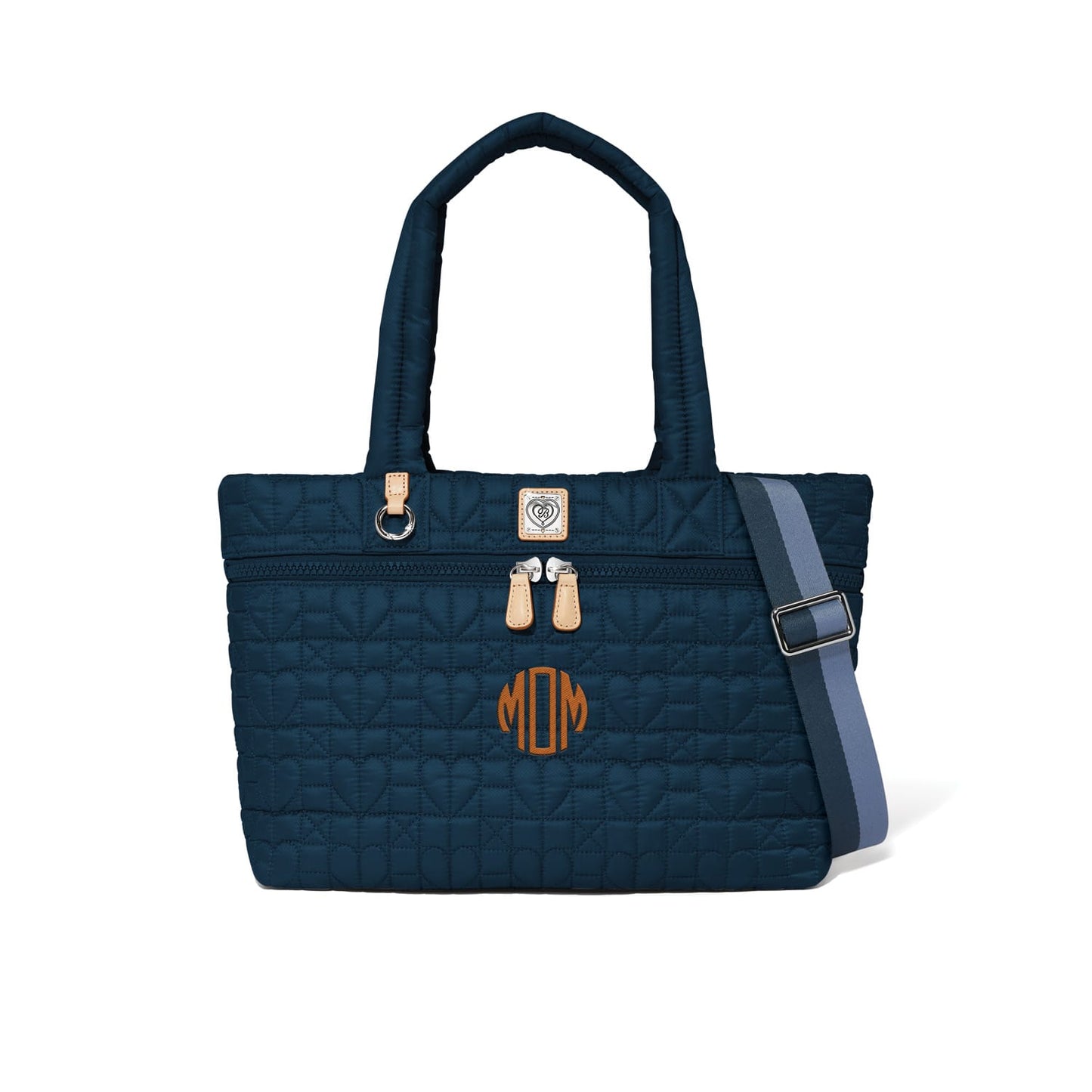 Brighton quilted navy tote handbag with MOM monogram, tan leather accents, and striped crossbody strap on a white background