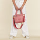 Model with a Brighton pink quilted handbag featuring LOVE embroidery, heart charms, and striped adjustable crossbody strap