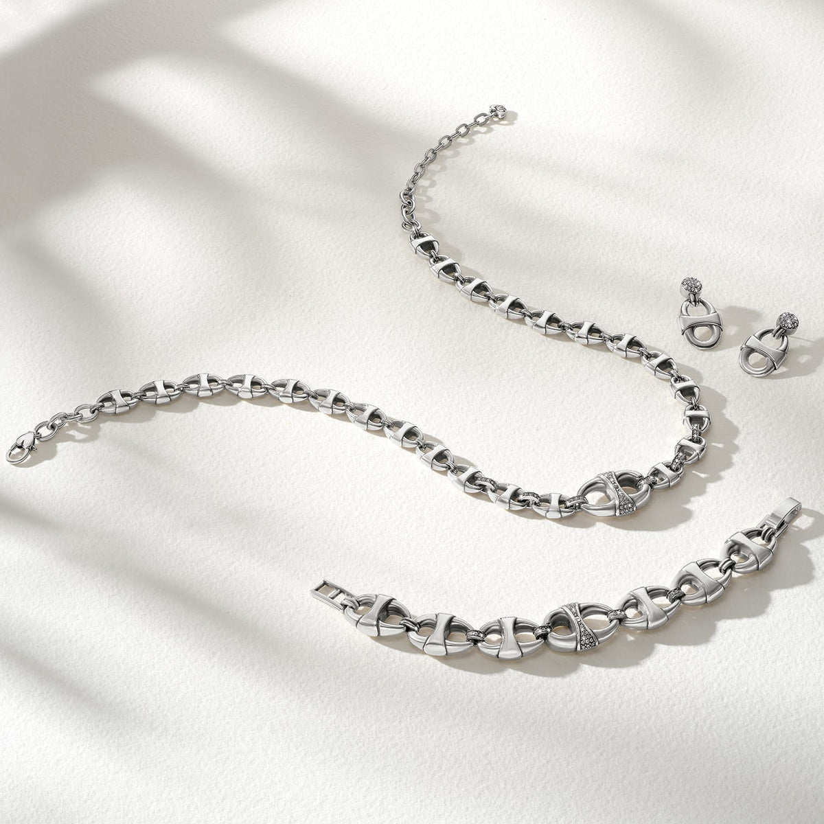 Brighton silver-plated jewelry set styled with matching chain link necklace, bracelet, and crystal drop earrings on neutral background