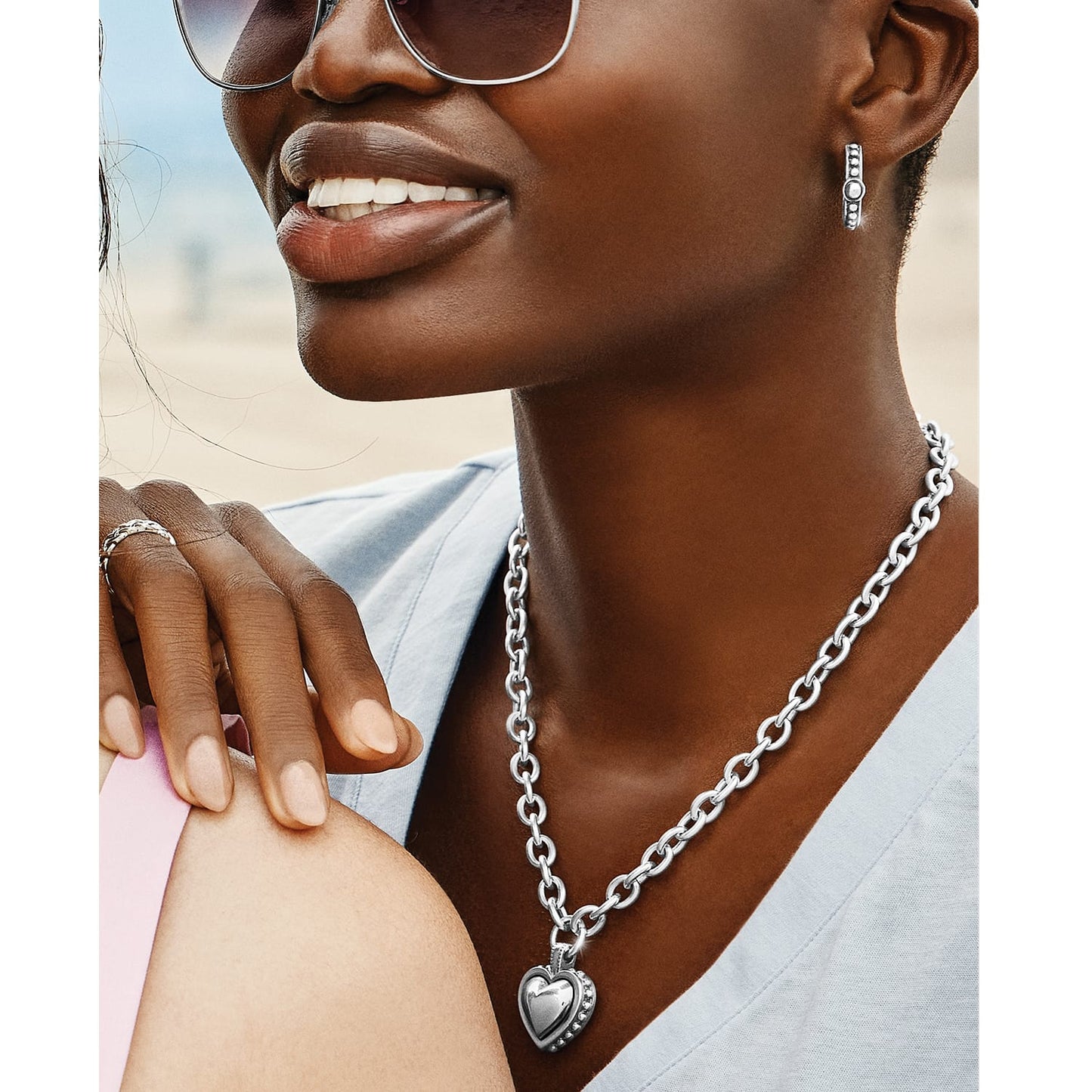 Model wearing a Brighton silver-plated chain necklace with heart pendant paired with coordinating silver-plated hoop earrings