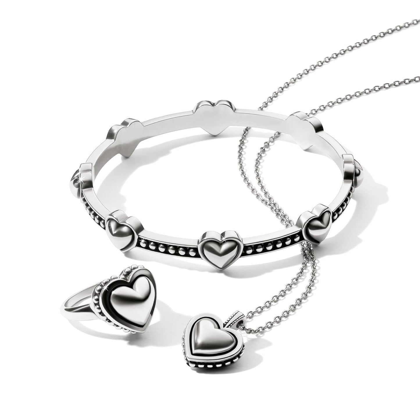 Brighton silver-plated jewelry set styled with heart-motif bangle, ring, and pendant necklace on a white background