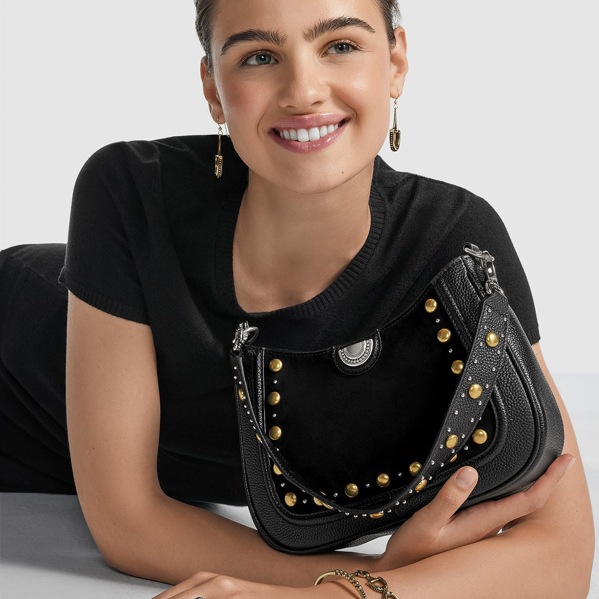 Model with a Brighton black leather handbag featuring gold and silver-tone studs and medallion accent