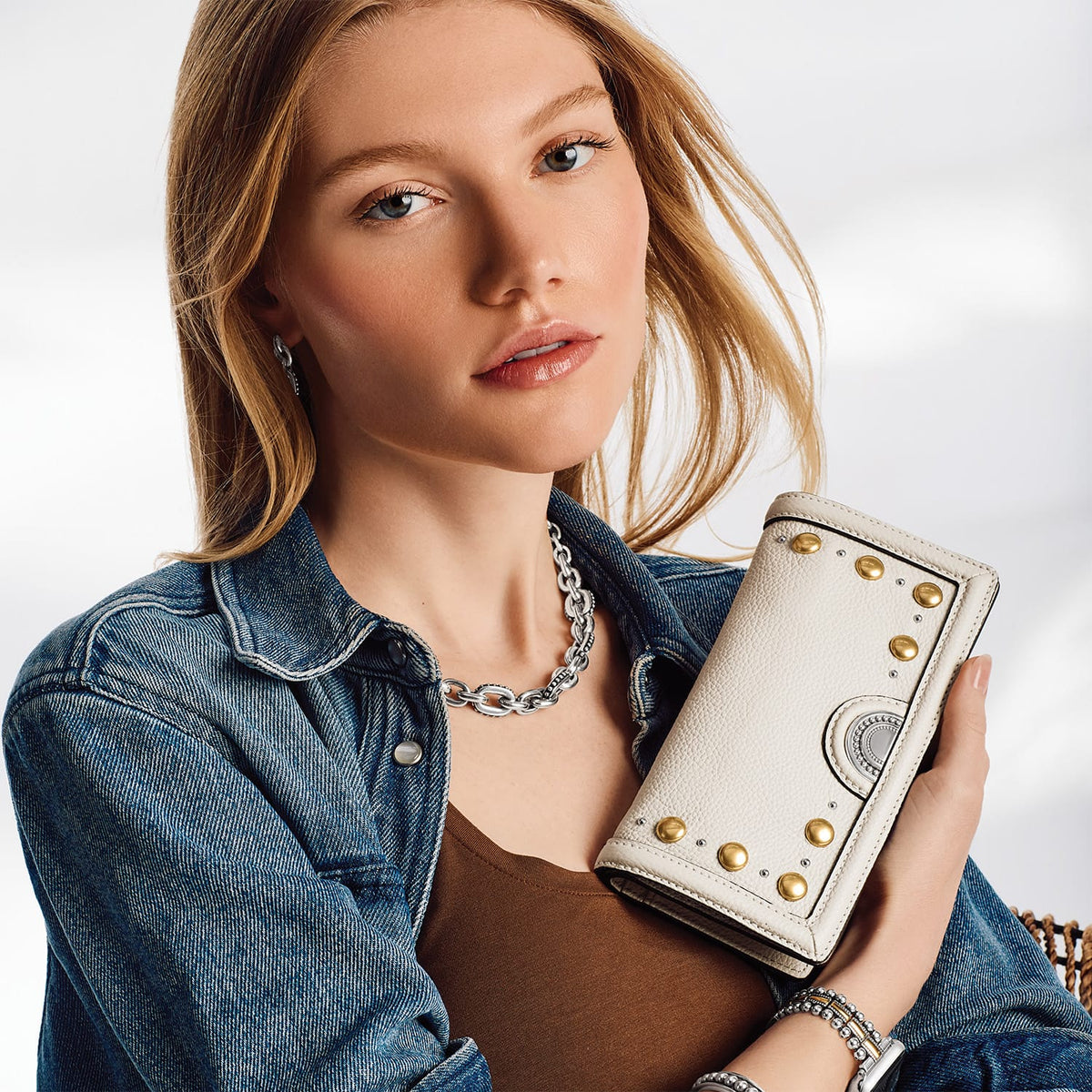 Model with a Brighton white leather wallet featuring gold and silver-tone studded accents and medallion detail