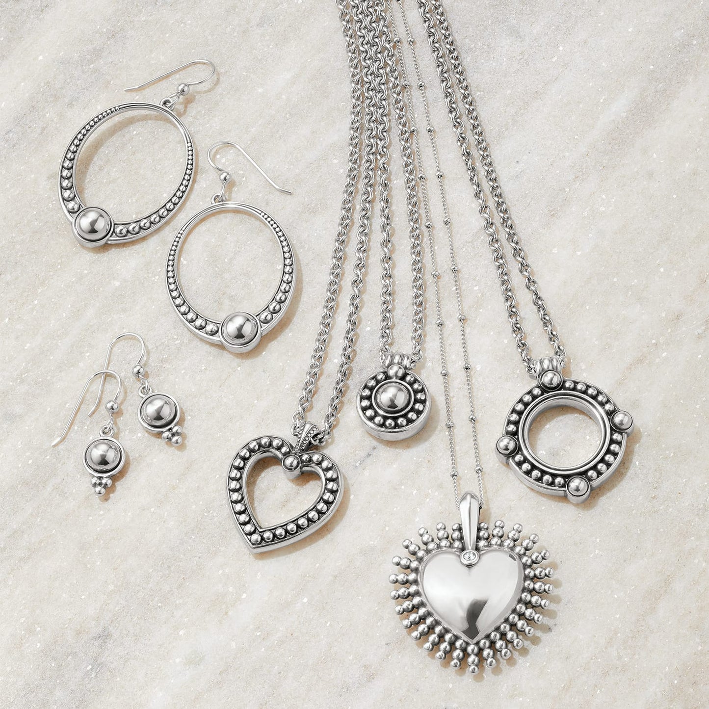 Brighton silver-plated jewelry set styled with hoop earrings, drop earrings, and heart pendant necklaces on stone background