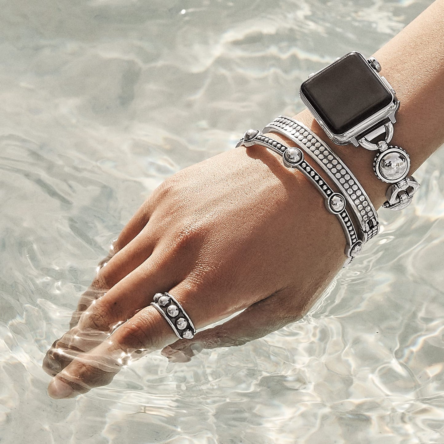 Model wearing Brighton silver-plated beaded bangle bracelets and a matching ring with a smartwatch, submerged in water