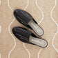 Brighton black leather woven mules styled with a patterned neutral rug backdrop featuring branded insoles
