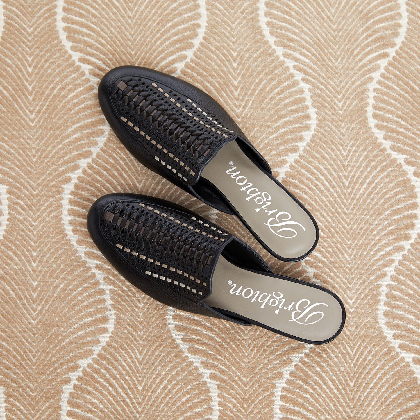 Brighton black leather woven mules styled with a patterned neutral rug backdrop featuring branded insoles