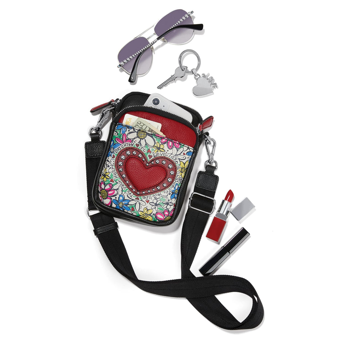Brighton crossbody bag with floral print and red heart, styled with sunglasses and other accessories on white background
