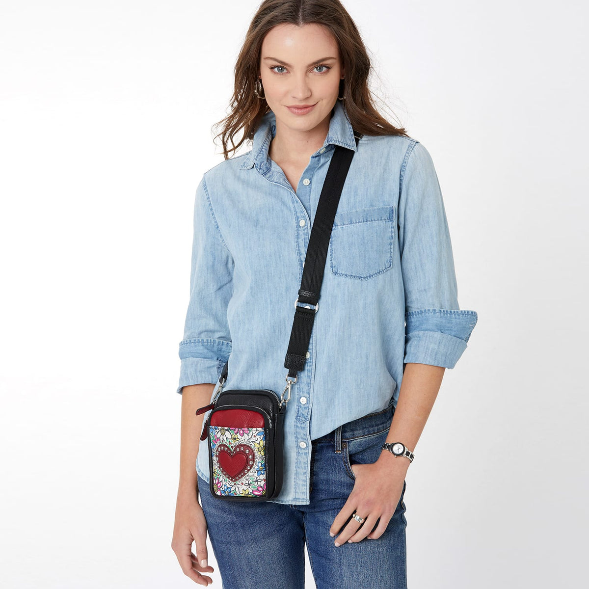 Model with a Brighton crossbody handbag featuring red heart appliqué, floral print, and black adjustable strap