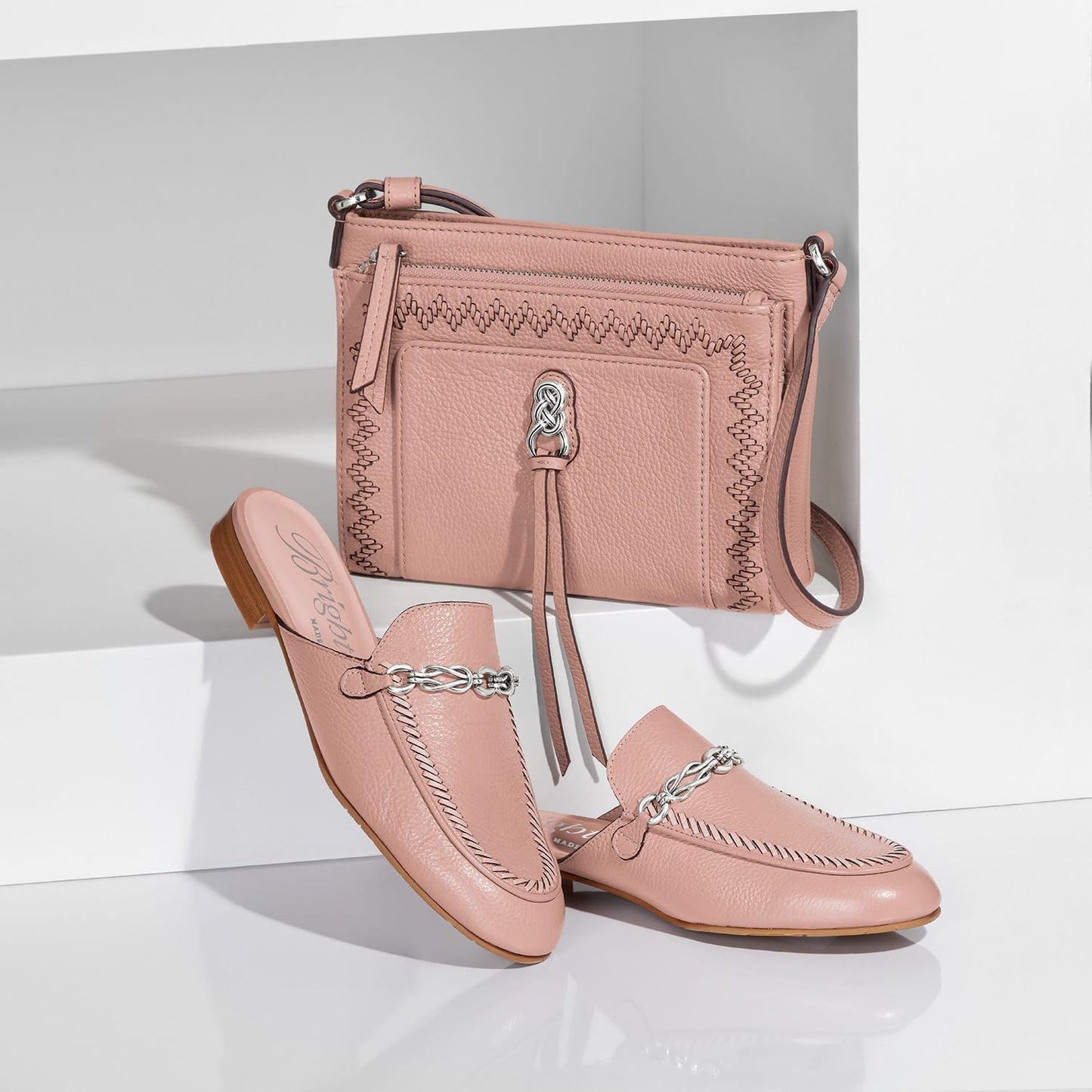 Brighton pink leather crossbody handbag styled with matching leather mules featuring silver-tone knot hardware on white background