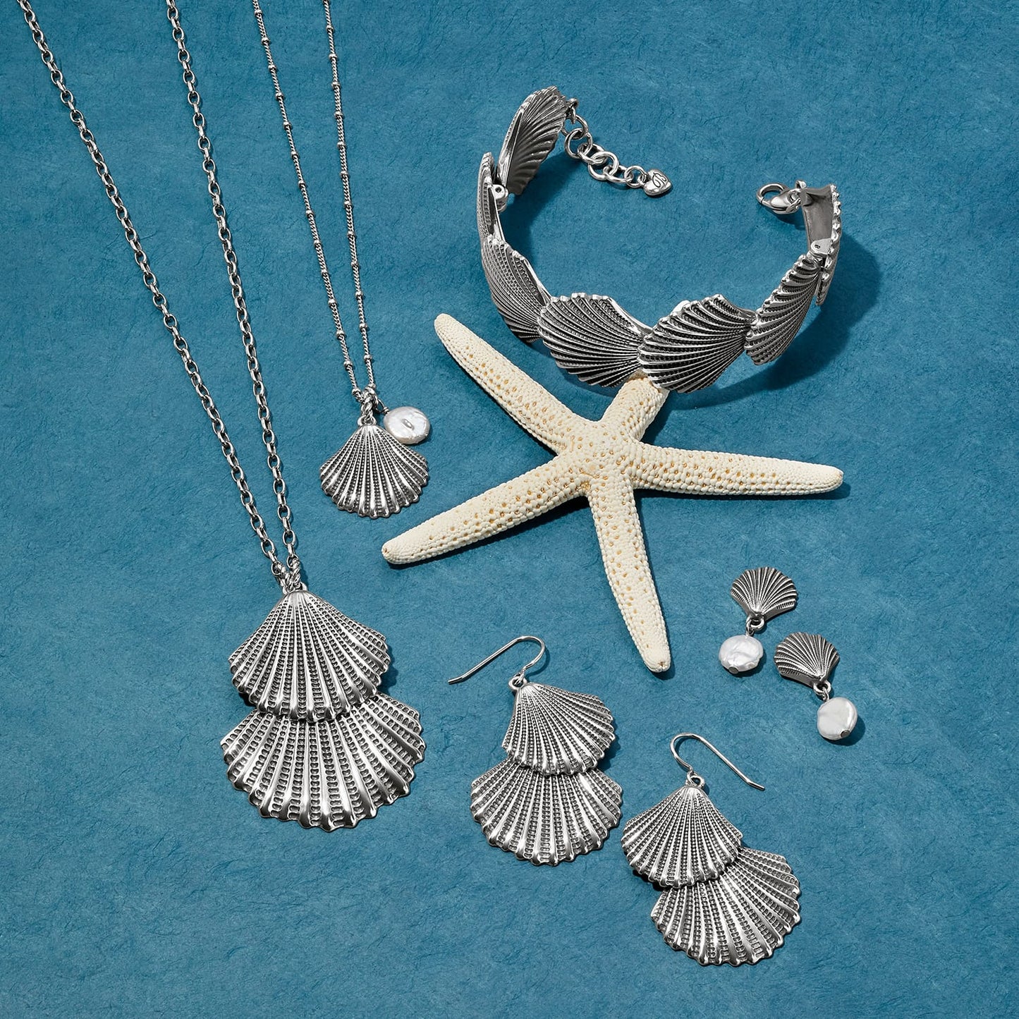 Brighton silver-plated shell jewelry set styled with a starfish and pearl accents on a blue background