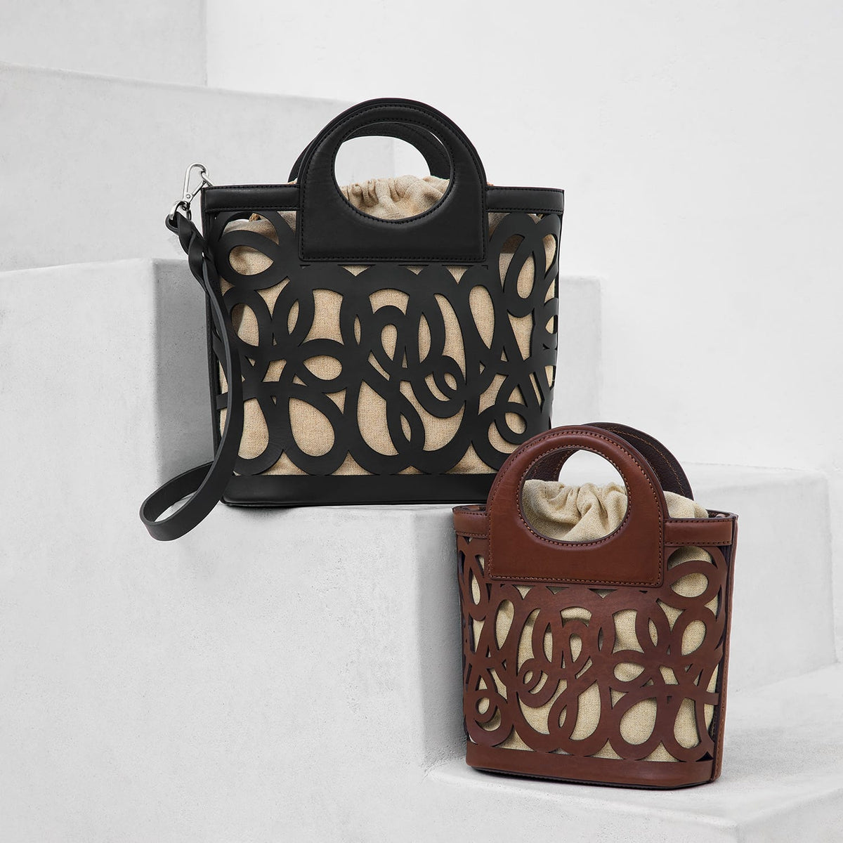 Brighton handbags in black and brown leather with cutout swirl designs over linen interiors on a white background
