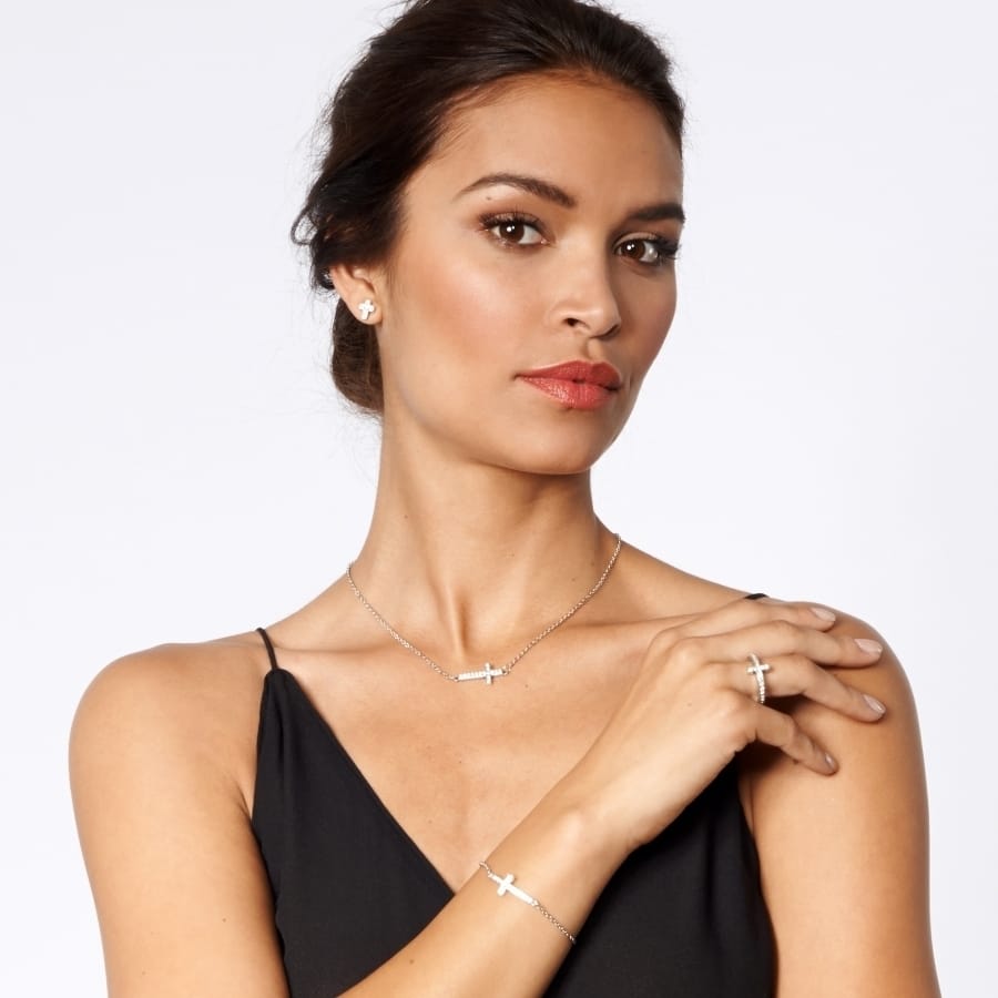 Model wearing a Brighton silver-plated cross necklace with coordinating Brighton accessories including bracelet, ring, and earrings