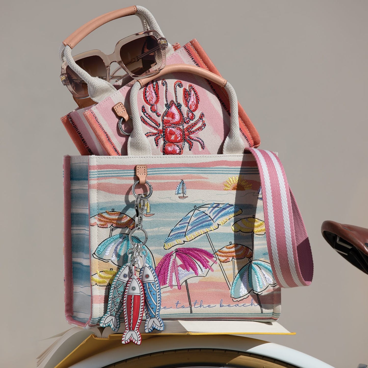 Brighton canvas tote with beach umbrella print, styled with sunglasses and fish charms among other accessories