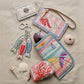 Brighton accessories styled with seashells and fish keychain, featuring illustrated lobster, seashell, and beach prints on sand