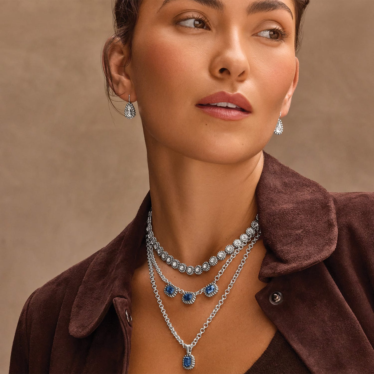 Model wearing Brighton silver-plated layered necklaces with blue and clear crystals paired with matching crystal drop earrings