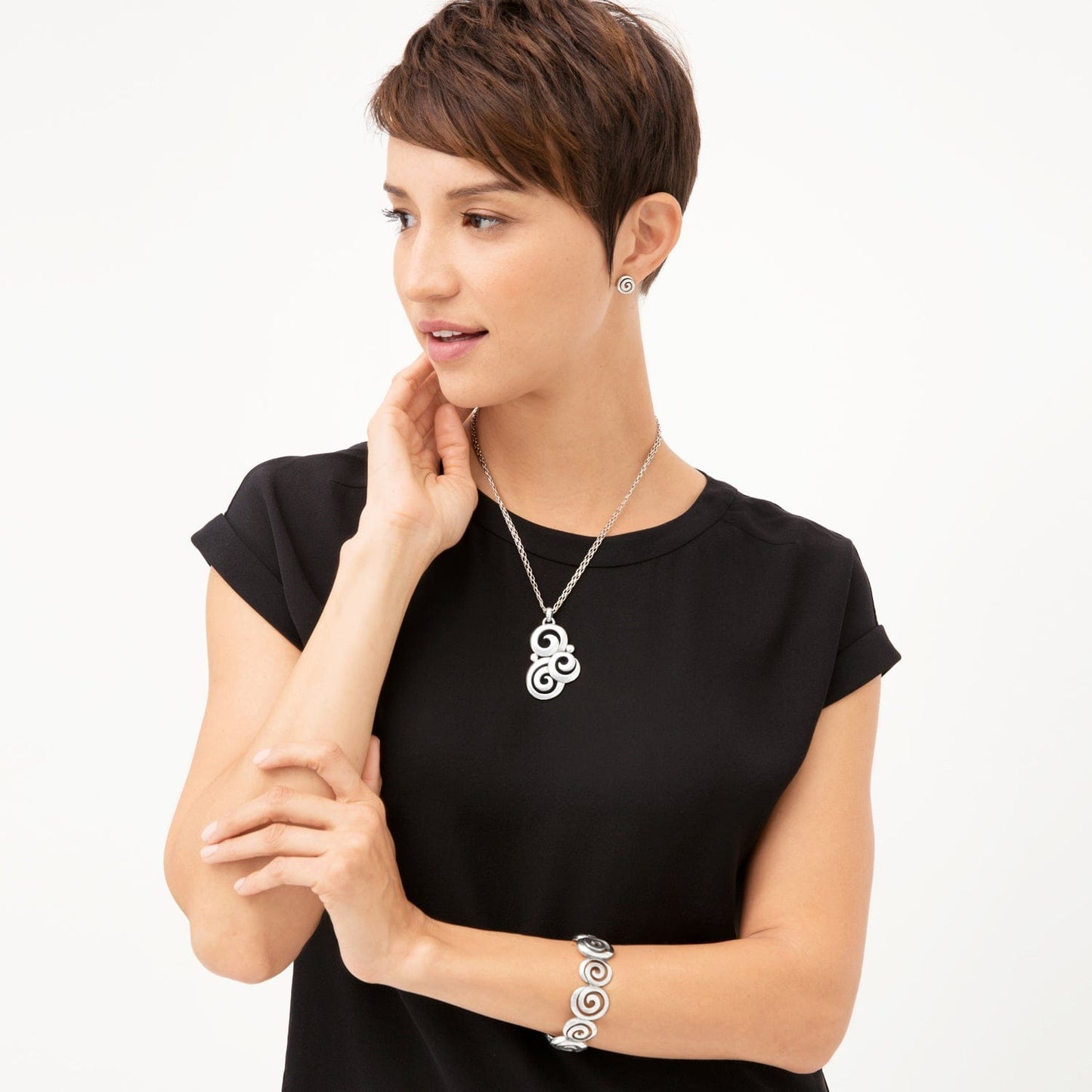 Model wearing a Brighton silver-plated swirl pendant necklace with coordinating Brighton stud earrings and swirl bracelet